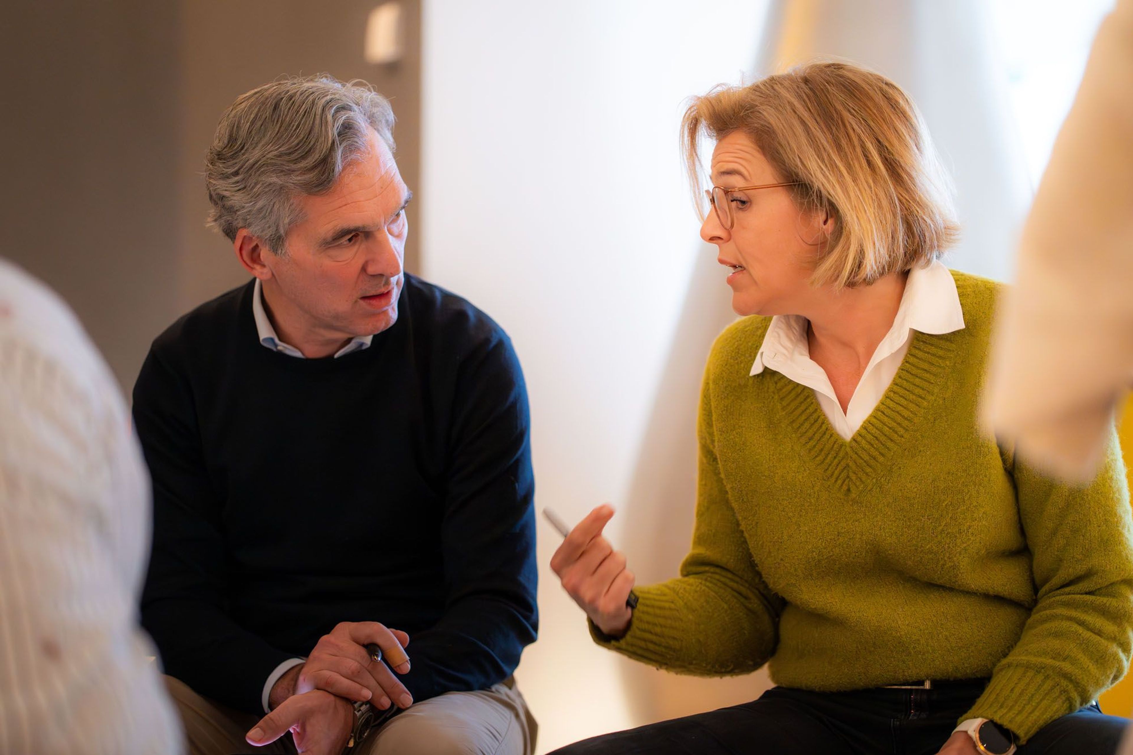 Twee mensen in gesprek, zittend, in een moderne ruimte.