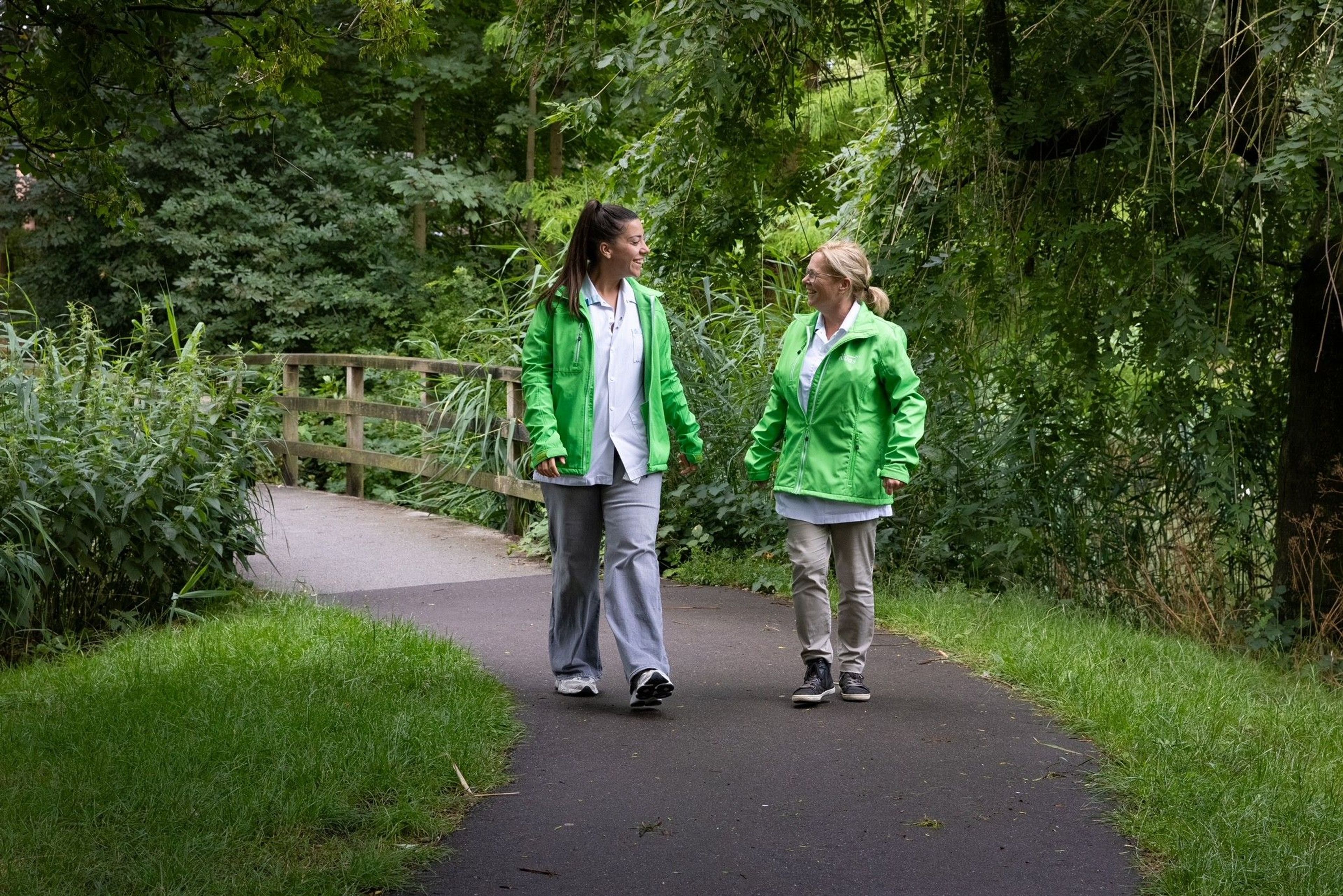 Twee vrouwen in groene jassen wandelen in het park.