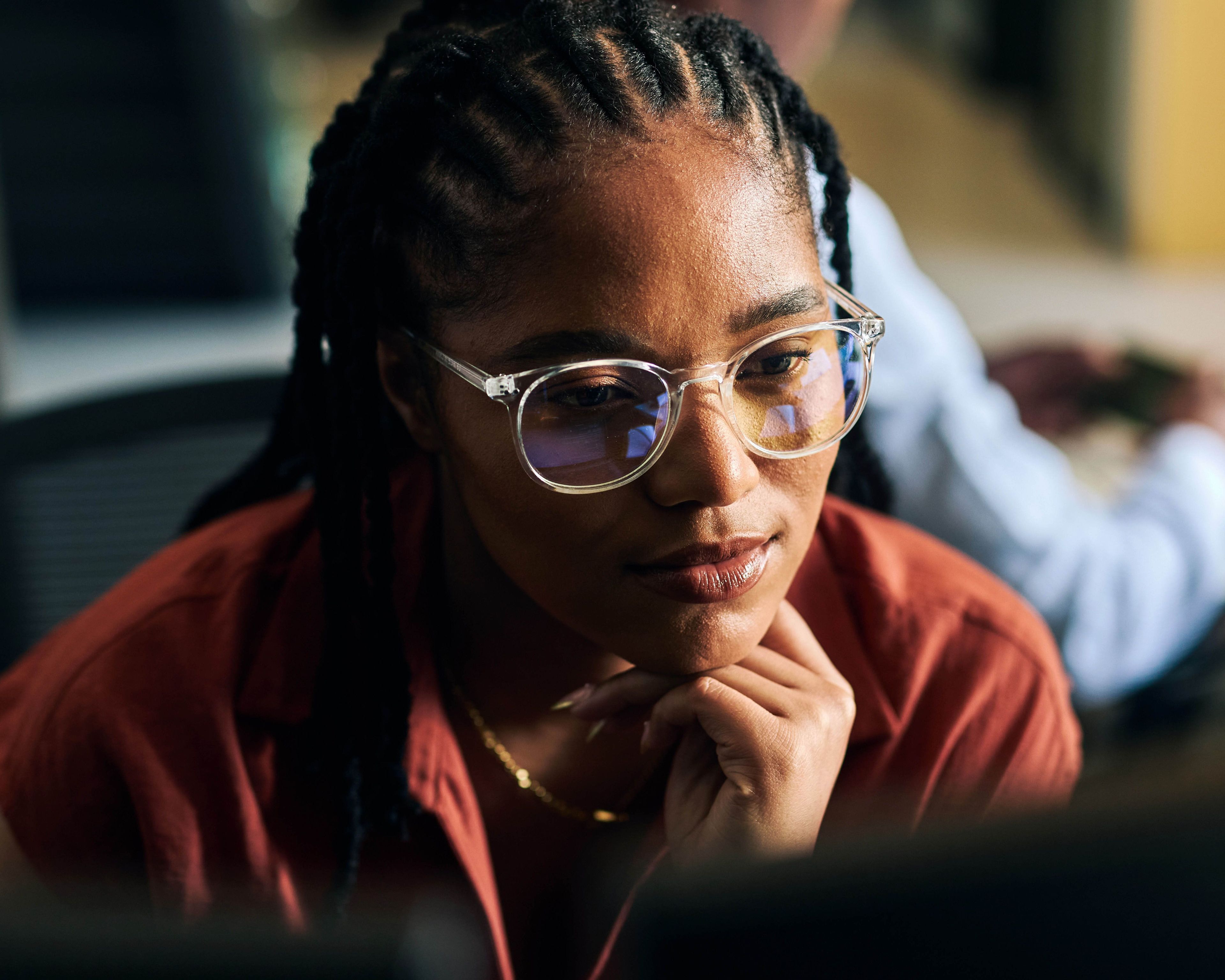 Vrouw met bril en vlechten, geconcentreerd achter computer.