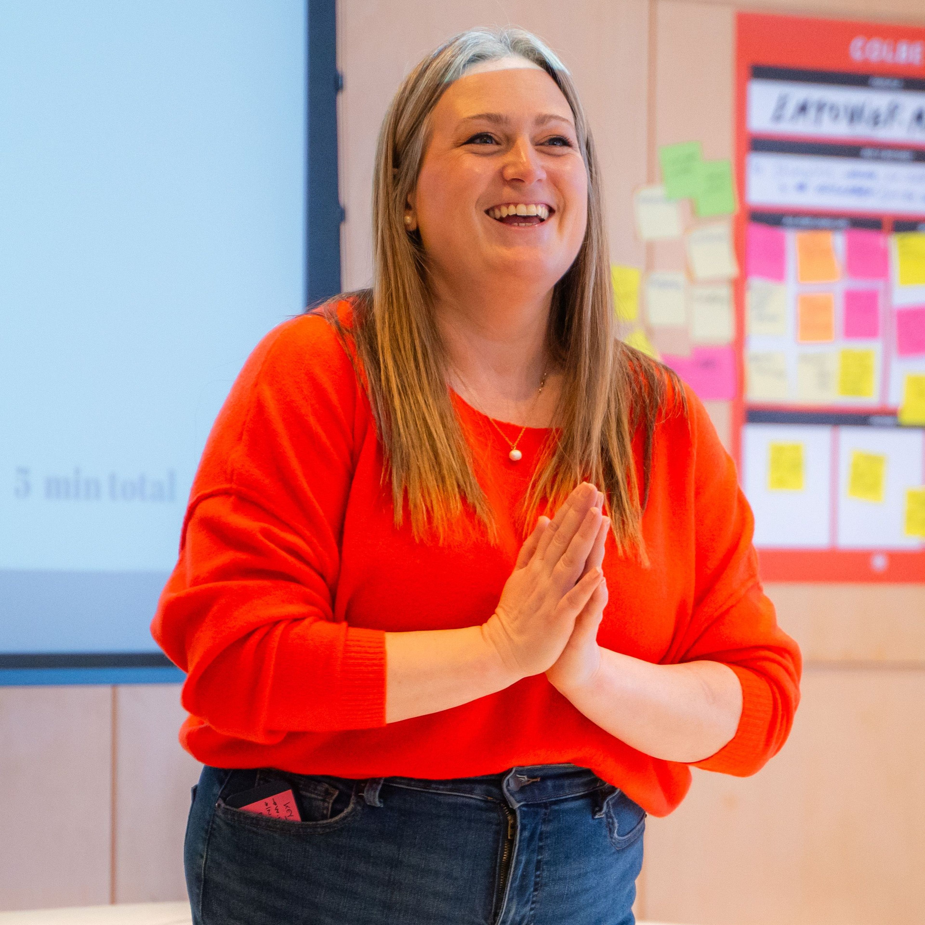 Vrouw in oranje trui glimlachend op een podium.