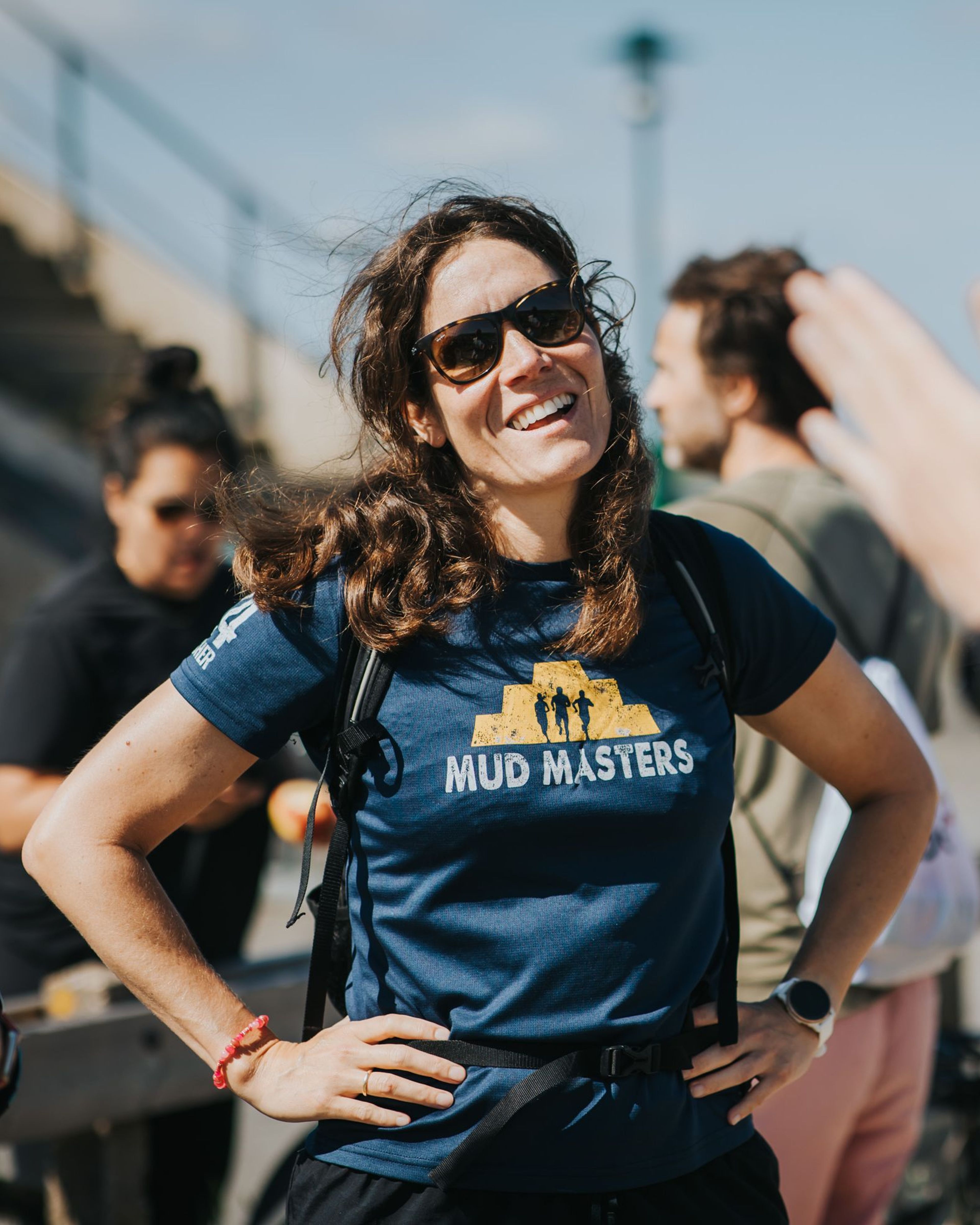 Vrouw in Mud Masters shirt met zonnebril en lach.