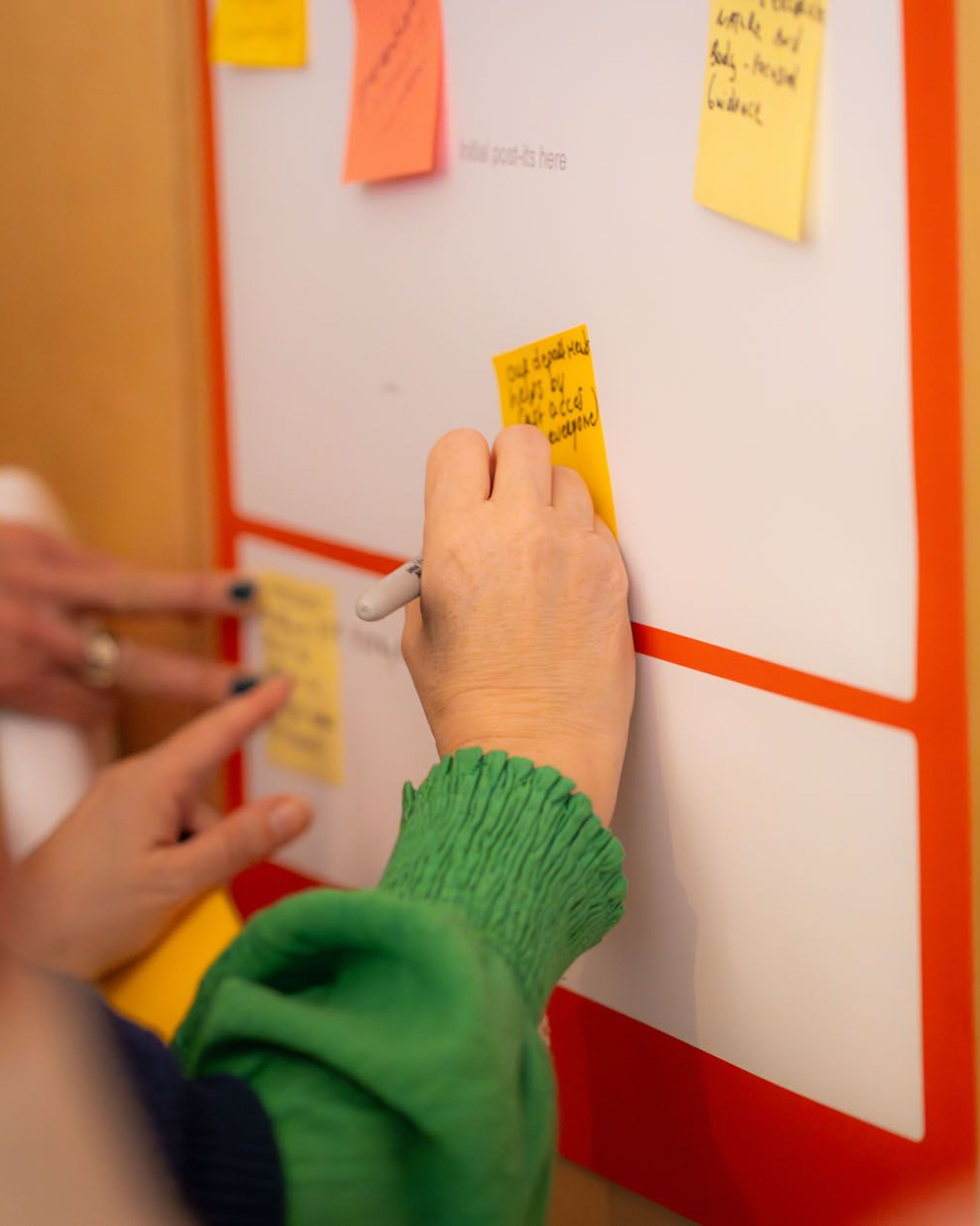 Handen schrijven op een whiteboard met post-its.
