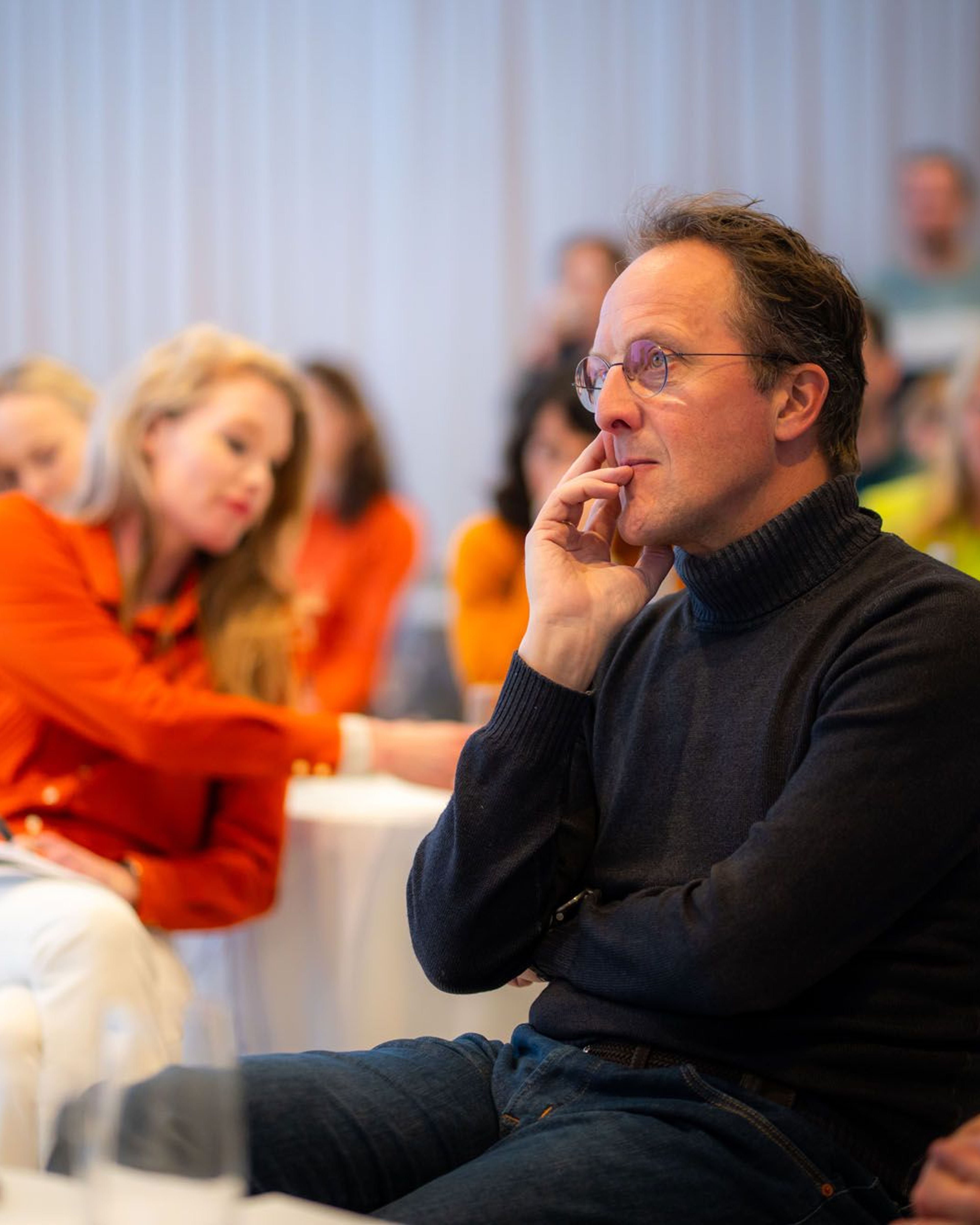 Man in een grijze trui, luisterend naar een presentatie.