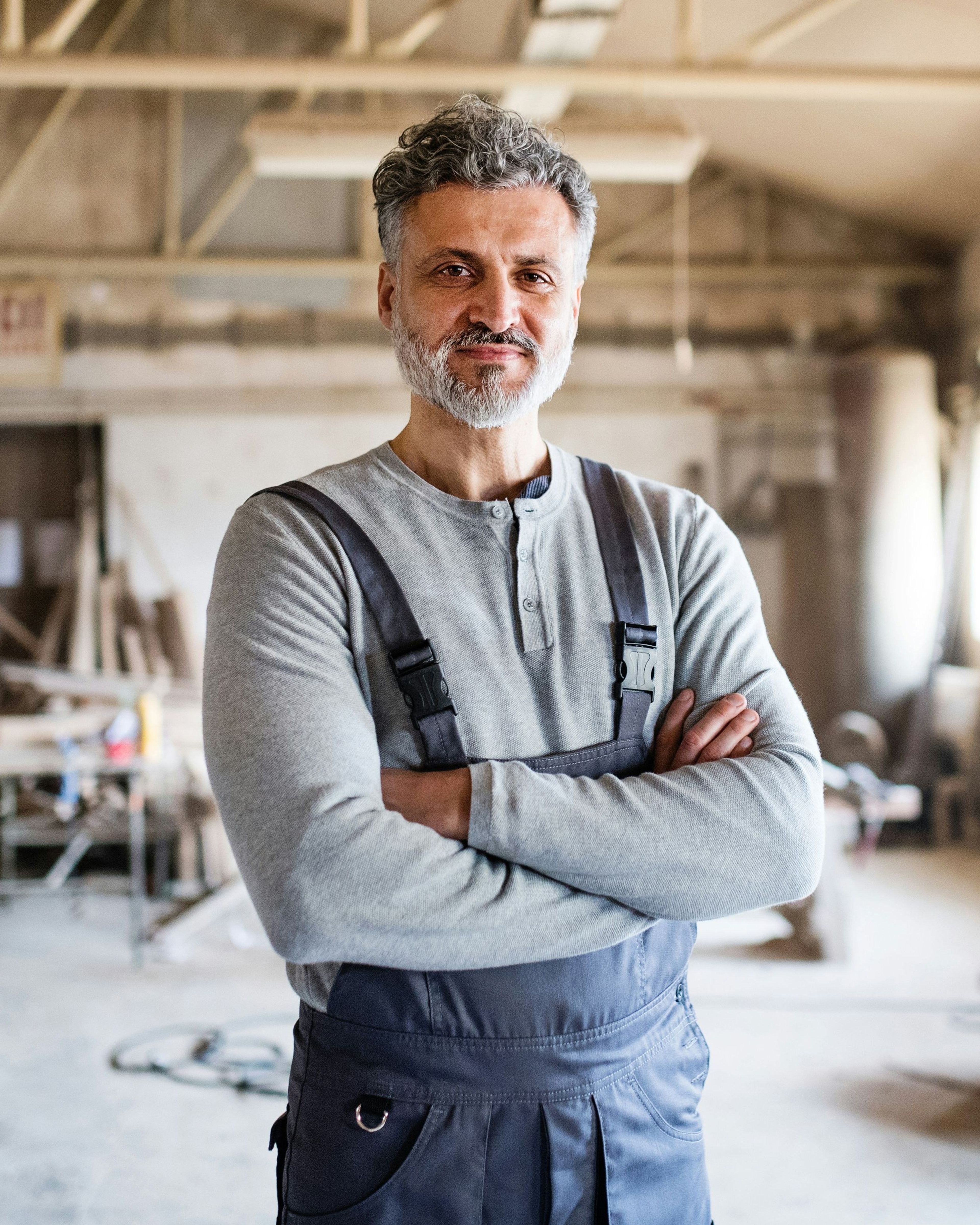 Man in een werkplaats met overalls en een glimlach.