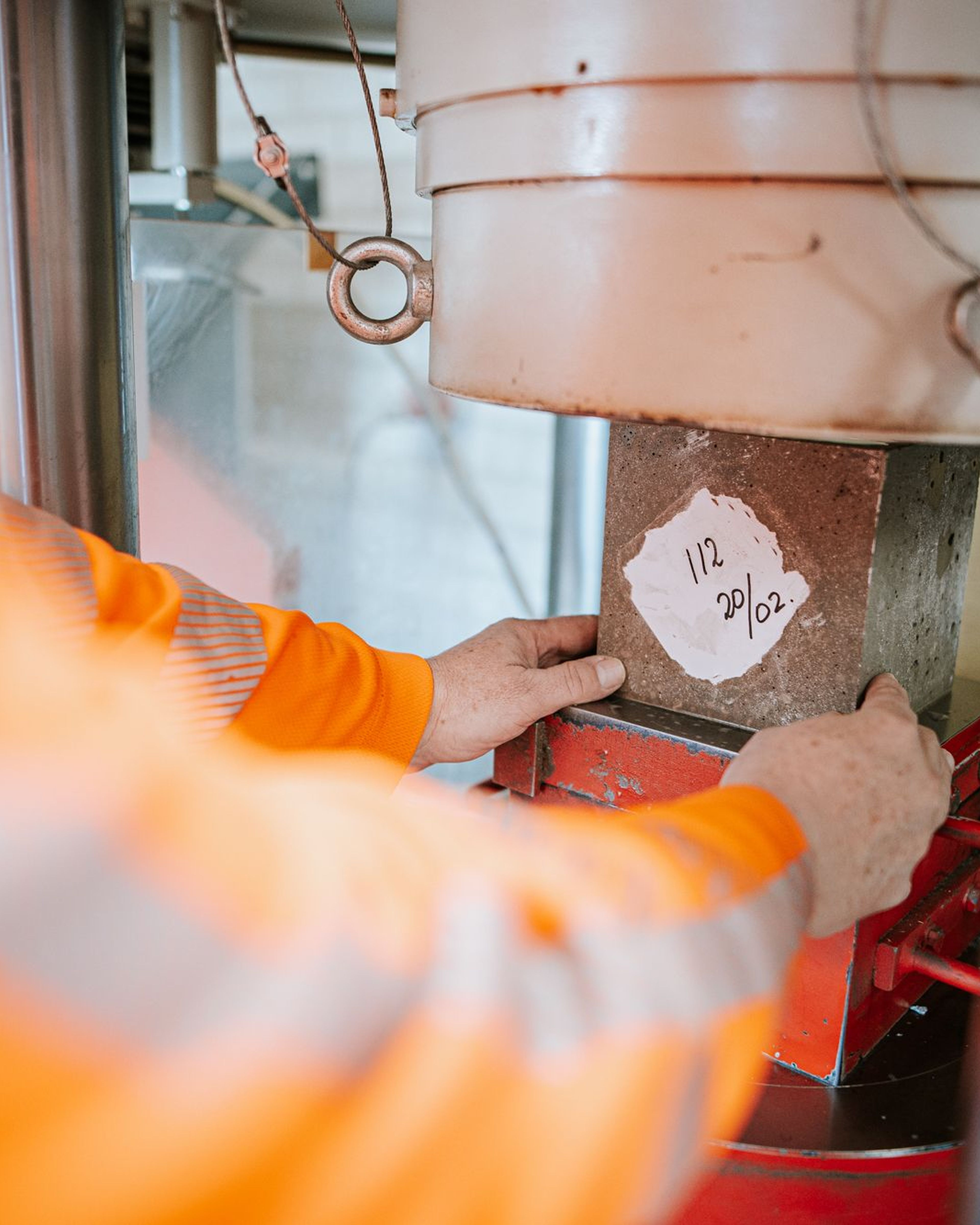Werknemer test betonsterkte met persmachine.
