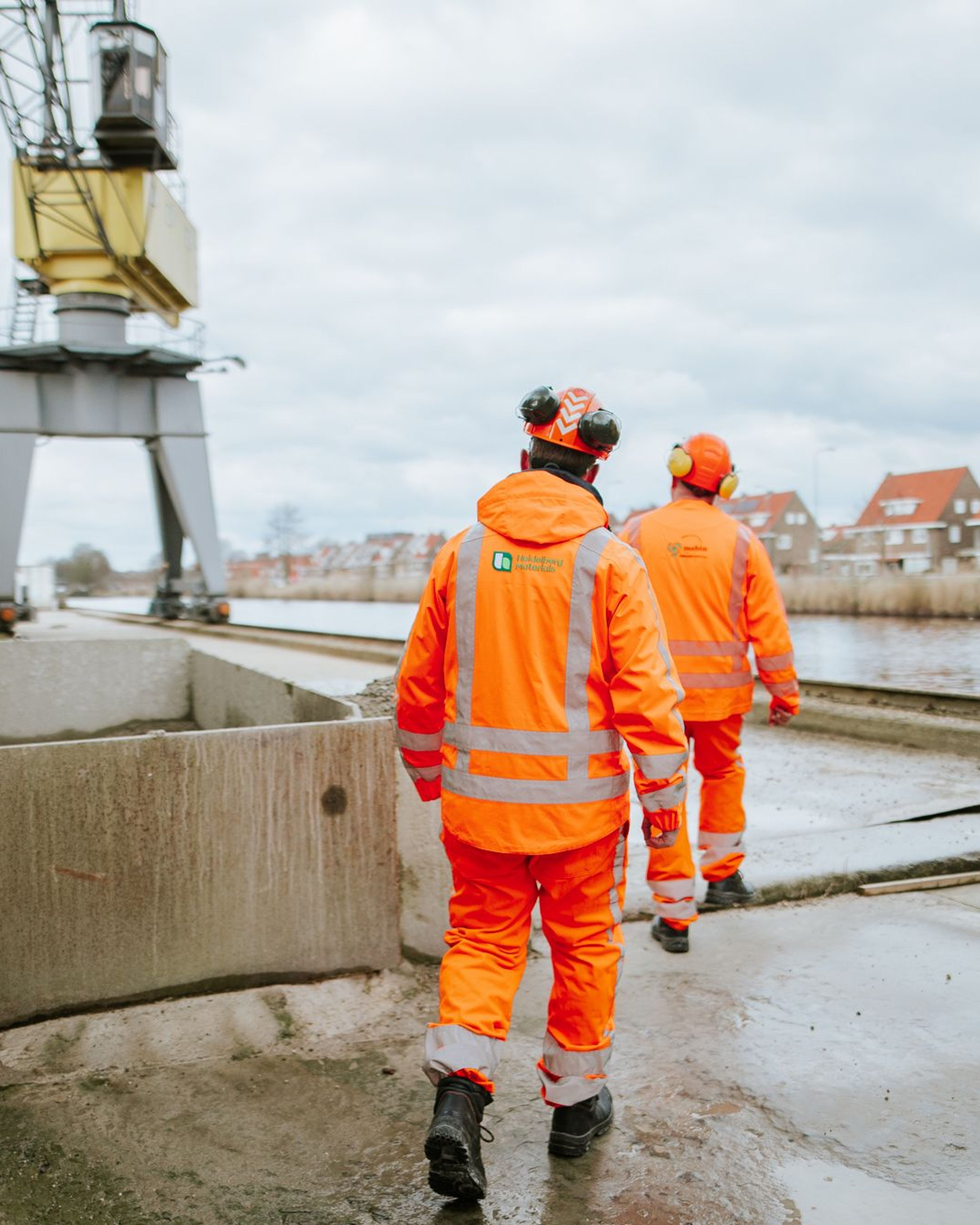Werkers in oranje veiligheidskleding bij een haven.