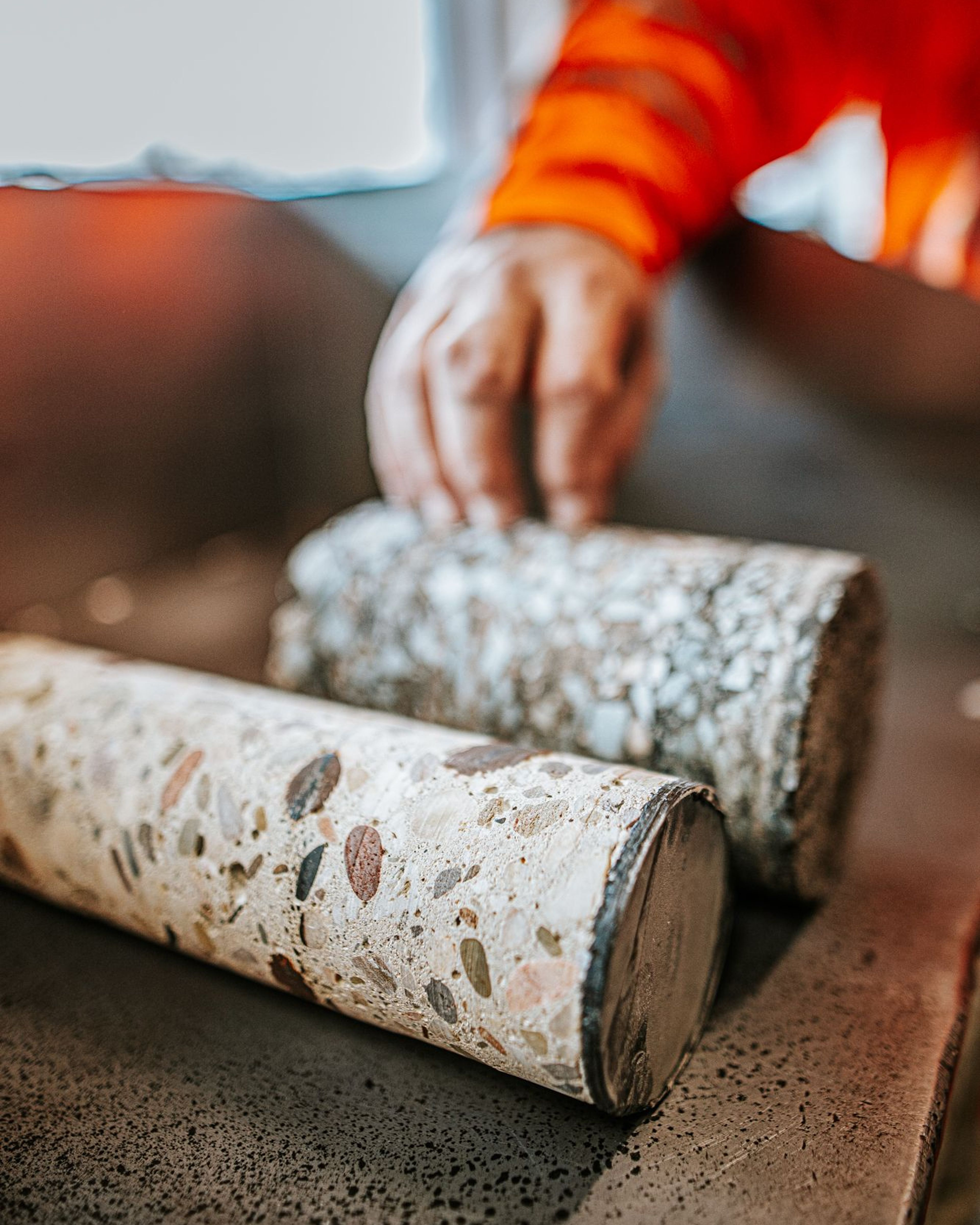 Betonnen staven liggen op een tafel, hand in beeld.