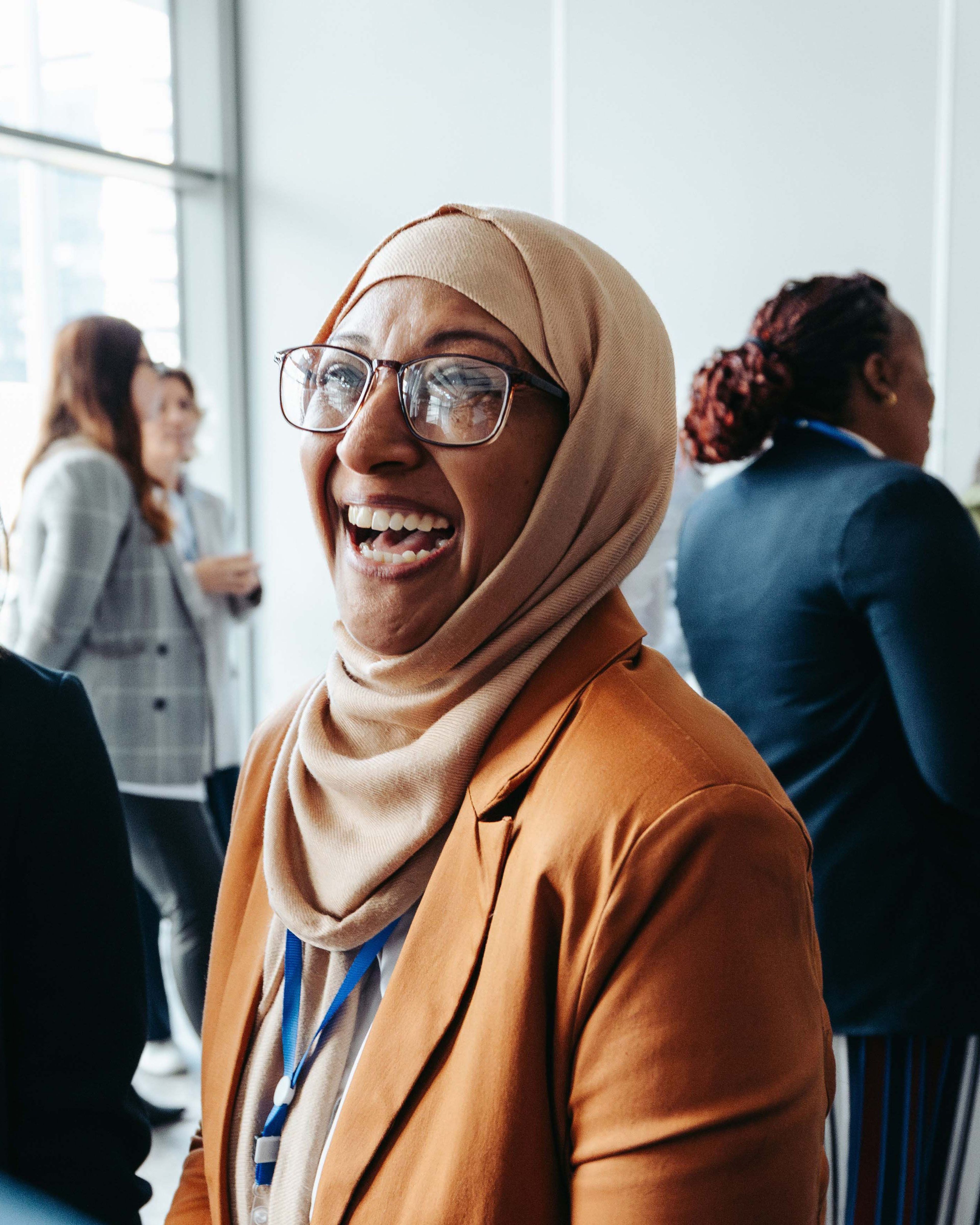 Vrouw in hijab lacht tijdens een bijeenkomst.