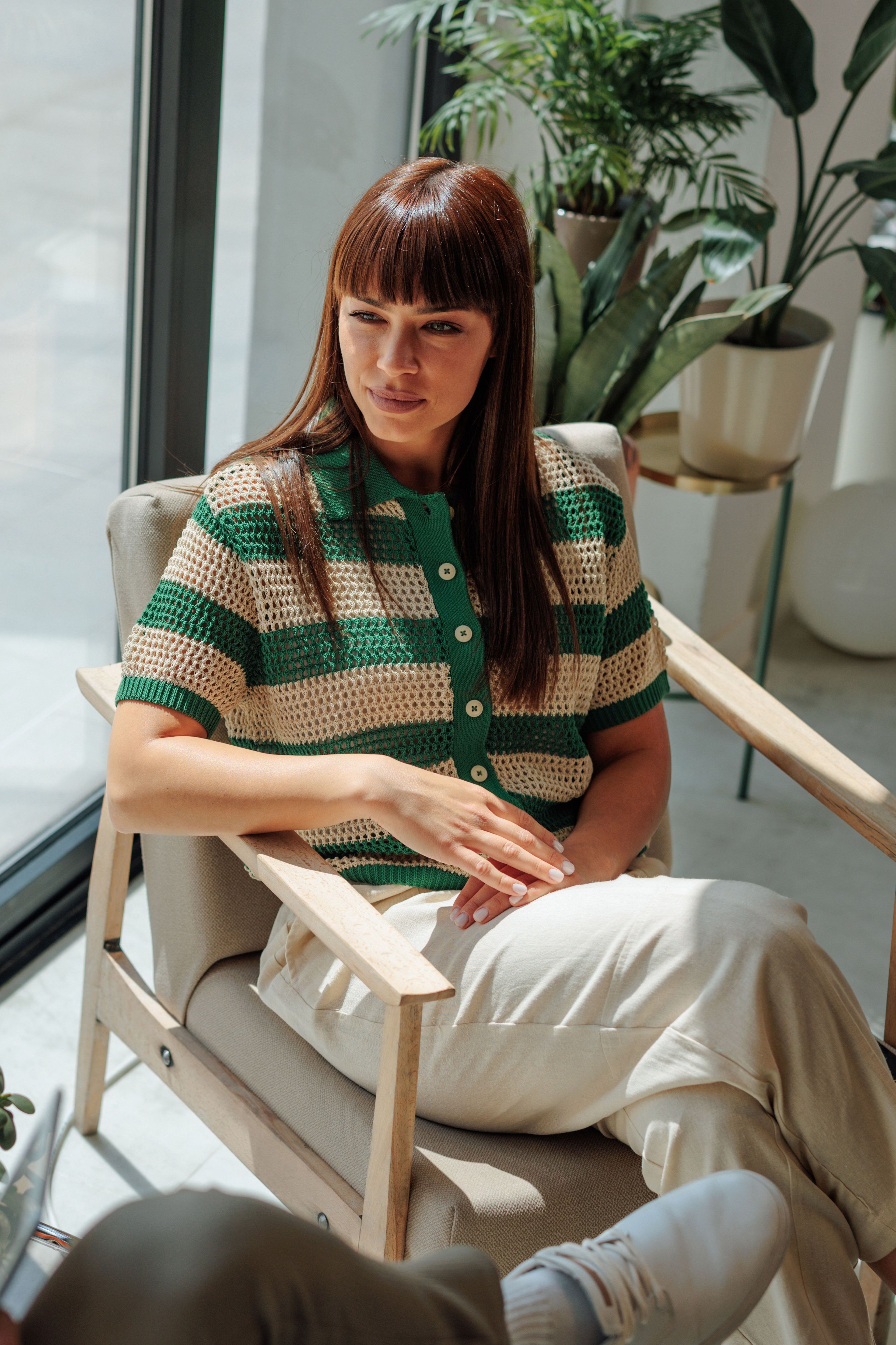 Vrouw in groene en beige gestreepte trui, zittend in stoel.